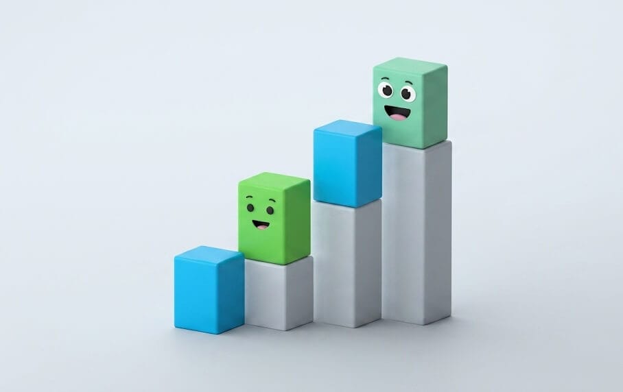 3D illustration of a bar chart with two green smiling building blocks on top of two columns, and two blue blocks on top of the two shorter columns. This symbolizes progress and successful steps.